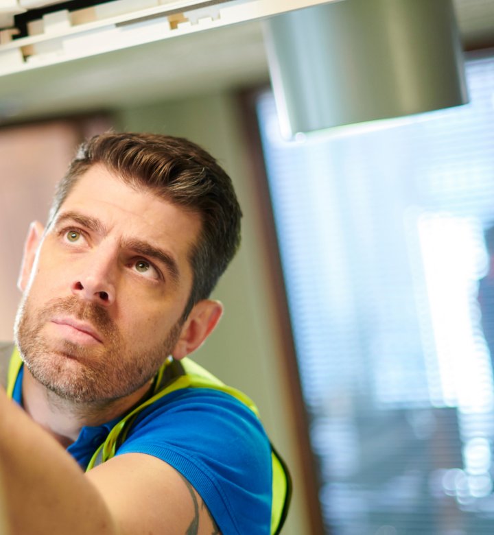 Man in high visibility vest inspecting indoor ceiling lighting
