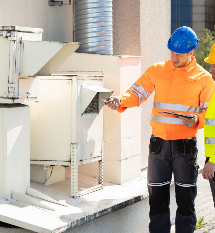 Two men in high visibility jackets and hard hats inspecting equipment outdoors