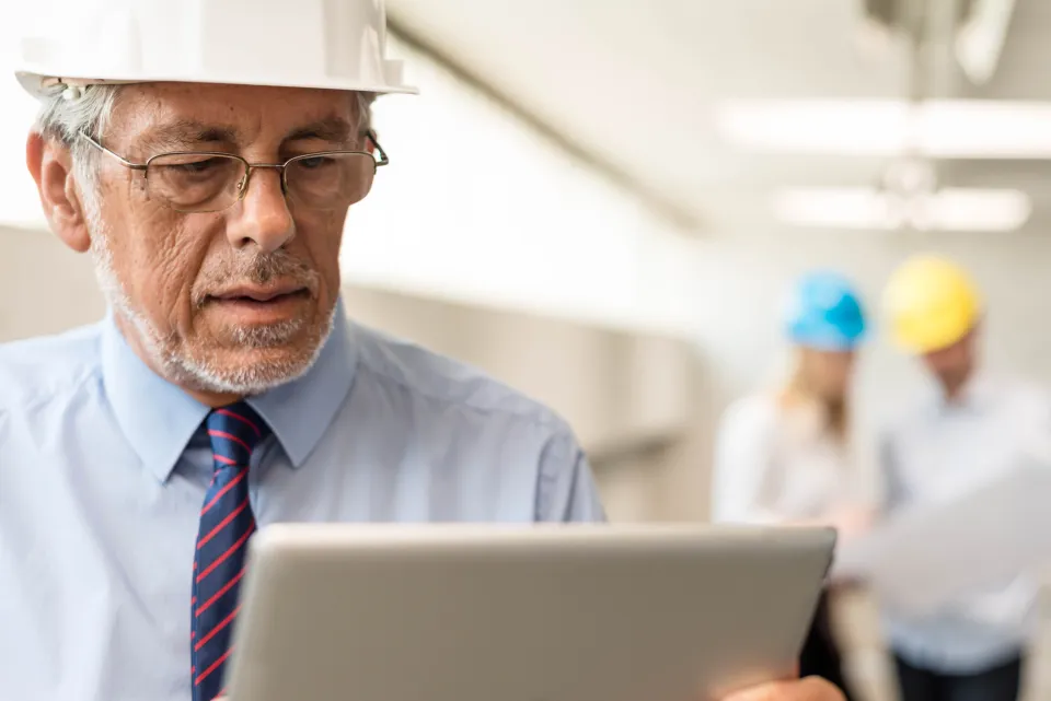 Man in business clothing and safety hat reading on a tablet