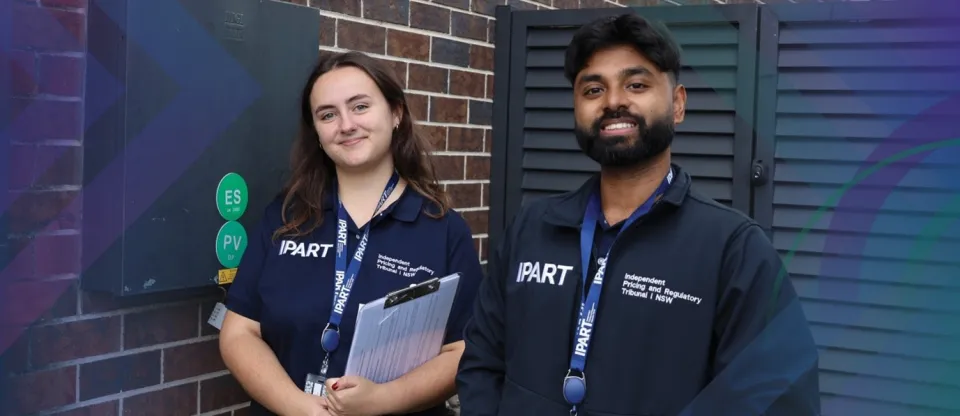 2 IPART Officers smiling wearing an IPART shift and a name lanyard, holding a notepad