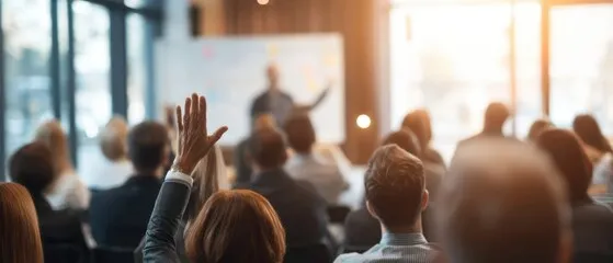 Audience watching a presentation. One audience member has their hand raised.
