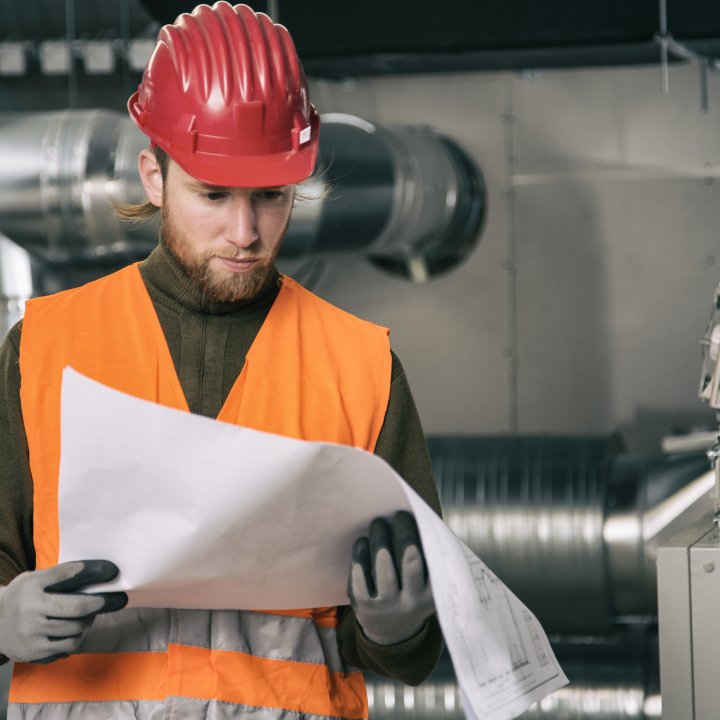 Man in hard hat and high visibility vest reading printed plans in factory