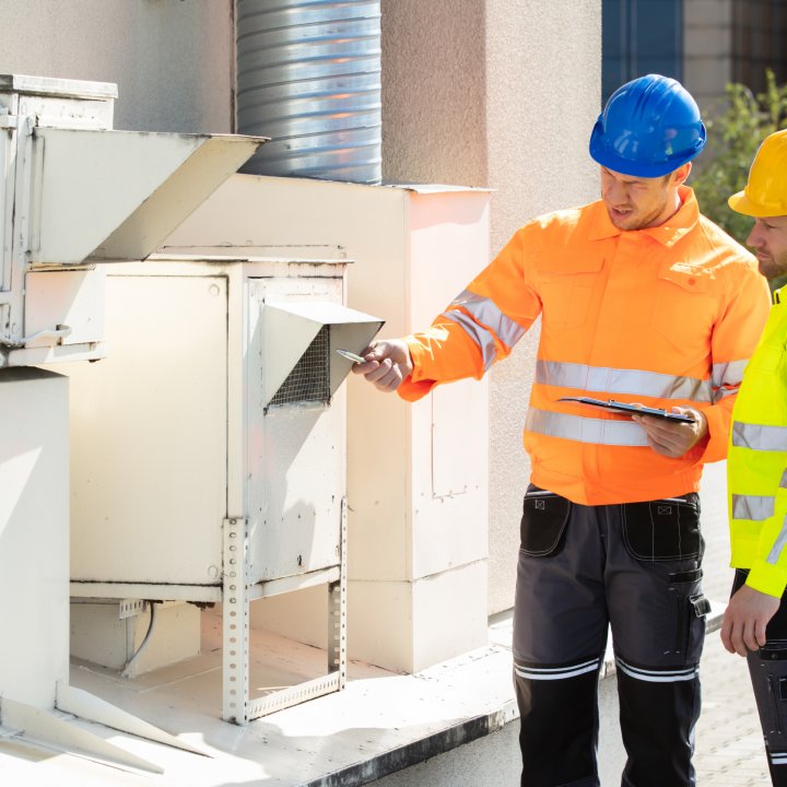 Two men in high visibility jackets and hard hats inspecting equipment outdoors