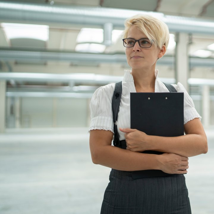 Woman with clipboard standing inside large empty warehouse