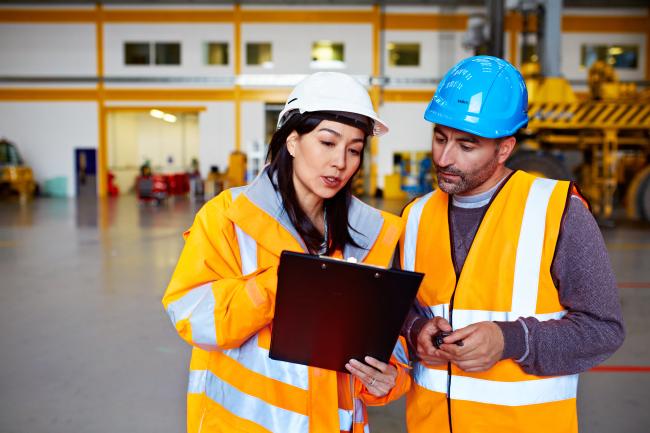 Woman and man wearing safety gear, looking at a document together in a workplace