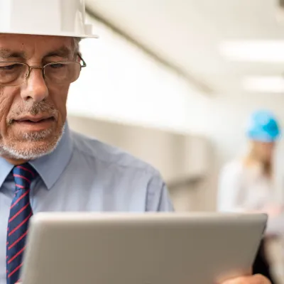Man in business clothing and safety hat reading on a tablet